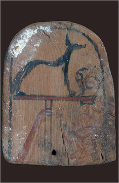 Wooden top to a police standard depicting a figure kneeling beneath an image of the god Wepwawet on a stand. Found in the Sanctuary of the Main Chapel.